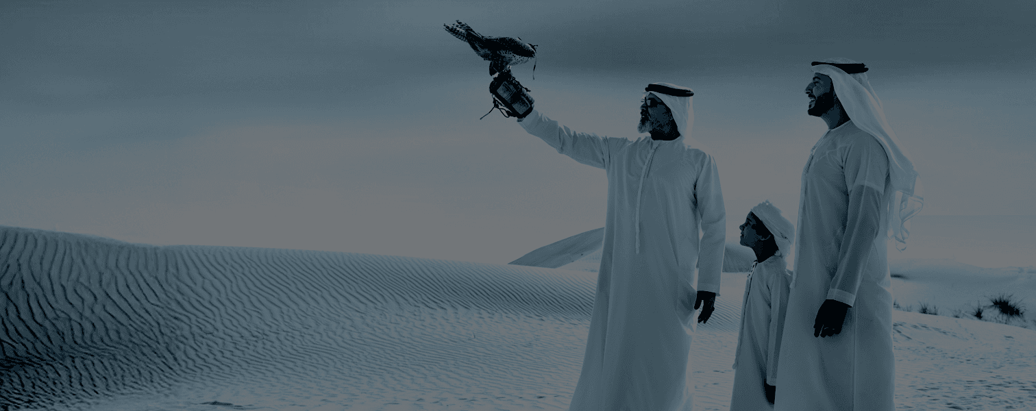 Desert landscape with three men in traditional Arab clothing, one holding a falcon on his gloved hand, under a cloudy sky